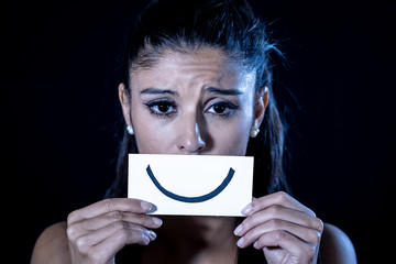 Young woman suffering from depression hiding her sadness and sorrow behind a drawn smile