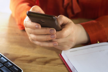 Close up shot of businesswoman using smartphone. Front view of girl in ginger blouse holding modern cell phone with both of her hands.