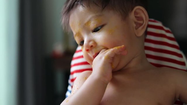 cute baby using finger hand in mouth itchy gum with food puree dirty on face
