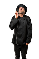 Chef man In black uniform with fingers crossing and wishing the best. Making a wish. on isolated white background