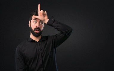 Handsome man with beard making loser sign on black background