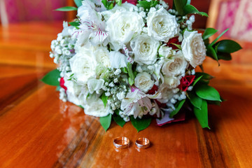 Beautiful wedding rings lie on wooden surface against background of bouquet of flowers. Declaration of love, spring. Wedding card, Valentine's Day greeting. Wedding rings. Wedding day details