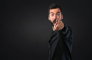 Handsome man with beard pointing to the front on black background