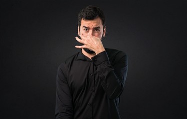 Handsome man with beard making smelling bad gesture on black background