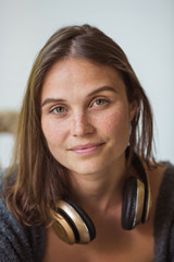 Naklejka premium Portrait of a young beautiful woman looking at the camera with golden headphones around her neck