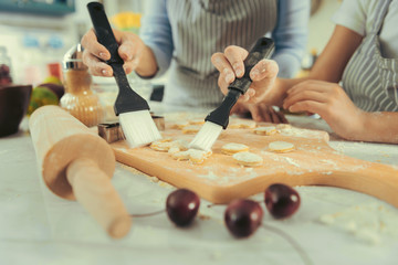 Handmade sweets. Close up of mother and daughter glazing cookies working on kitchen together