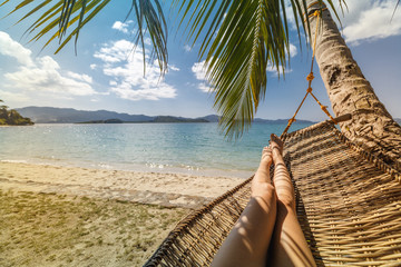 Sexy legs of a woman lying in a hammock on a beach by the open sea