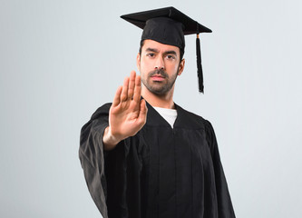 Man on his graduation day University making stop gesture with her hand denying a situation that thinks wrong on grey background