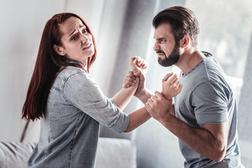 Help me. Cheerless unhappy young woman standing opposing her husband and being held by him while having a family quarrel