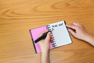 To do list in spiral notepad. Woman fills in to do list on wooden table, top view