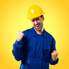 Young workman with helmet celebrating a victory and happy for having won a prize on yellow background