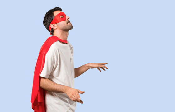 Superhero man with mask and red cape enjoy dancing while listening to music at a party on isolated blue background