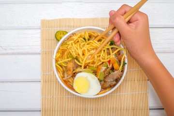 Boy hand holding chopsticks for eating Mee Rebus from white bowl on the table