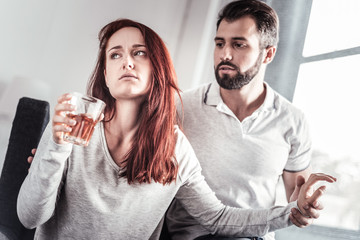 Leave me alone. Nice unhappy depressed woman holding a glass of whisky and turning away from her boyfriend while being addicted to alcohol