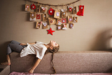 the advent calendar hanging on the wall. small gifts surprises for children. girl lies and looks at the calendar