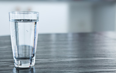 Glass of room temperature water on the black wooden table, kitchen.