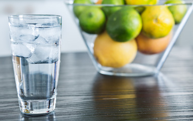 Glass of cold ice water with bowl of fruits on the background.