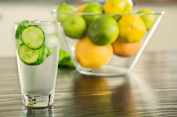 Glass of fresh cucumber water with bowl of fruits on the background.