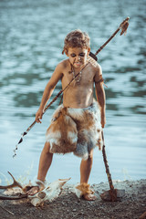 Angry caveman, manly boy with stone axe and bow hunting near river. Prehistoric tribal boy outdoors...
