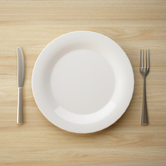 Top view of ceramic plate with fork and knife on wooden table. 3d rendering
