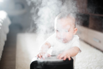 Little baby looks at the humidifier. Moisture in the house concept