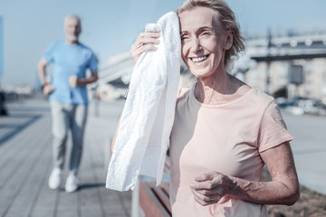 Making pause. Attractive female person keeping smile on her face and using towel while having rest