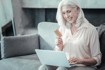 Online shopping. Joyful positive nice woman looking at the netbook screen and holding a credit card while doing online shopping