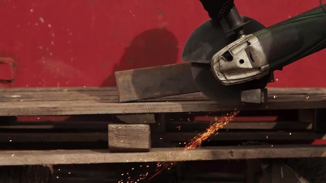 The manual machine for metal cutting works. Sparks fly to the parties. Working process of cutting of metal. The worker saws a detail. Quickly the disk rotates, bright sparks are scattered in the parti