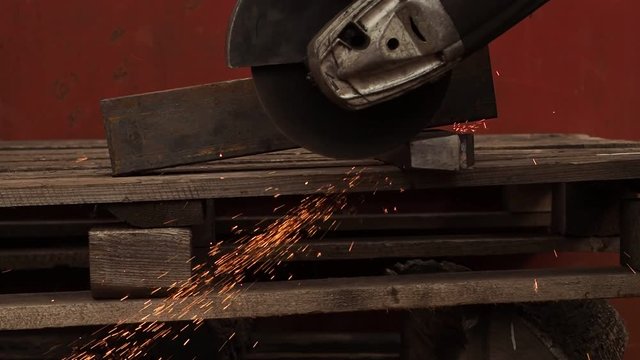 The manual machine for metal cutting works. Sparks fly to the parties. Working process of cutting of metal. The worker saws a detail. Quickly the disk rotates, bright sparks are scattered in the parti