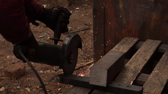 The manual machine for metal cutting works. Sparks fly to the parties. Working process of cutting of metal. The worker saws a detail. Quickly the disk rotates, bright sparks are scattered in the parti