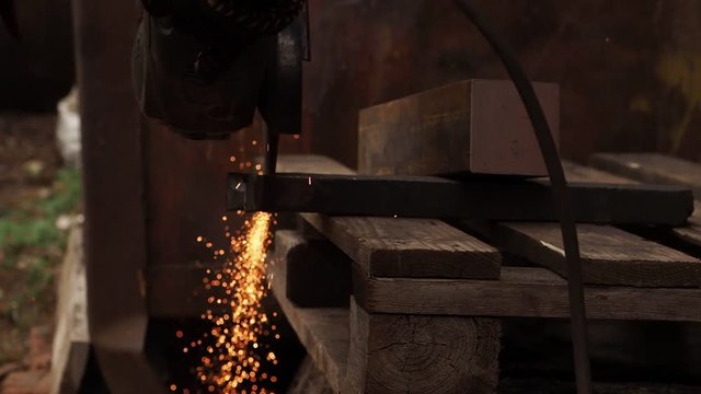 The manual machine for metal cutting works. Sparks fly to the parties. Working process of cutting of metal. The worker saws a detail. Quickly the disk rotates, bright sparks are scattered in the parti