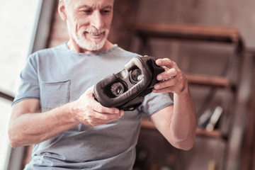 Powerful tool. Close up of virtual reality mask being kept in hands of joyful bearded man