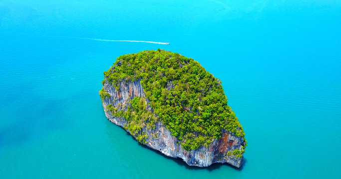 Isolated Rocky Tropical Island With Lush Greenery Surrounded by Turquoise Ocean Water and Boat Passing in Background - Aerial Overhead View - Thailand