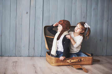Happy kid in pilot hat and little girl playing with old suitcase. Childhood. Fantasy, imagination. Travel concept