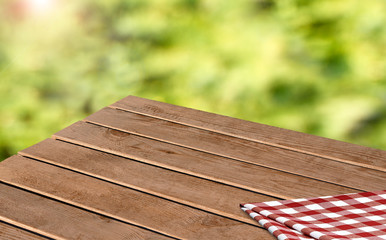 Perspective view of empty wooden table corner with tablecloth on blurry green grass background