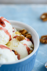 Vanilla ice cream with walnuts and fruit syrup in a blue bowl.