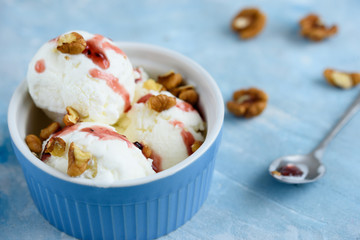 Vanilla ice cream with walnuts and fruit syrup in a blue bowl.