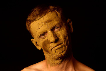 Face closeup portrait on black background. Dried clay on the face, cracked skin. Display of empty...