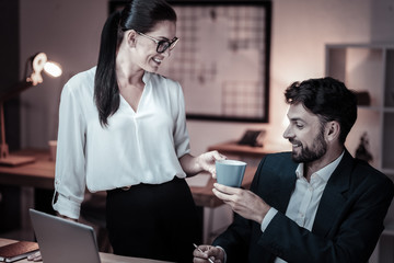 It is for you. Charming female keeping smile on her face and looking forward while standing near her boss