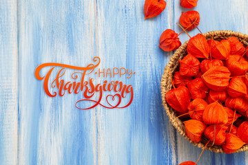 Thanksgiving - letters. Autumn background. Bright orange physalis berries on a blue woody background. Congratulations for the autumn holidays and thanksgiving day.