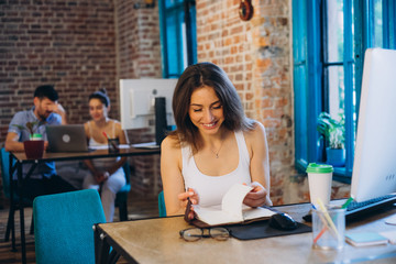 Portrait of a pretty young woman while sitting at the table with laptop computer and notebook at office. startup
