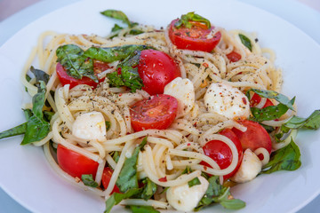 Spaghetti caprese of cherry tomatoes and mozzarella cheese with basil on a plate close-up