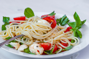 Spaghetti caprese of cherry tomatoes and mozzarella cheese with basil on a plate close-up