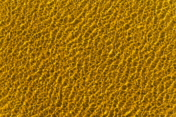 Sea bottom with golden sand in clear water with ripples, top view - beautiful sea background