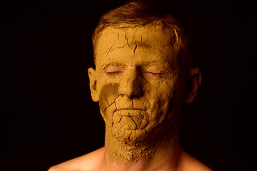 Face closeup portrait on black background. Dried clay on the face, cracked skin. Display of empty on the face.