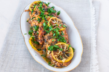 Chicken Francese, Italian-American dish - fried chicken breast in a sauce of lemon slices on a white plate.