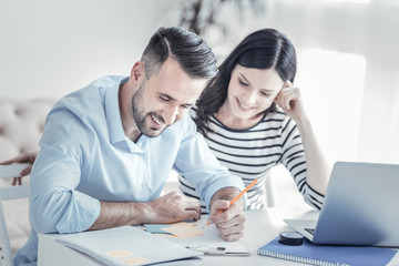 Obraz premium Being satisfied. Handsome male person expressing positivity while looking downwards, sitting at his workplace