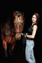 Portrait of smiling pretty woman standing by horse on the black background. Isolate