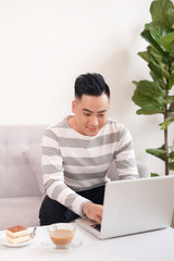 Man holding white cup of coffee and sitting with notebook on luxurious sofa in living groom.