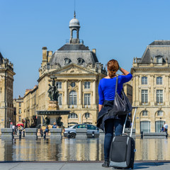 Obraz premium Woman with a suitcase on the Exchange Square, Bordeaux, France. Back view..